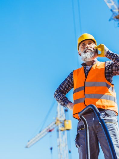 smiling-construction-worker-in-reflective-vest-and-hardhat-talking-on-smartphone.jpg